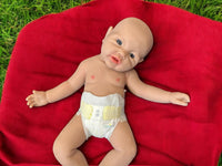 Thumbnail for A baby doll resting on a vibrant red blanket, showcasing its soft features and delicate clothing.