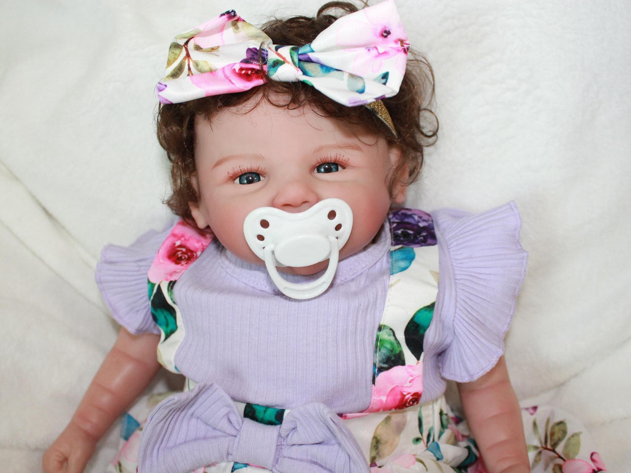 A baby doll wearing a purple dress and a decorative flower headband.