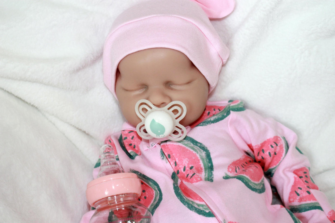 A baby doll holding a pacifier, dressed in a colorful outfit, with a gentle expression on its face.