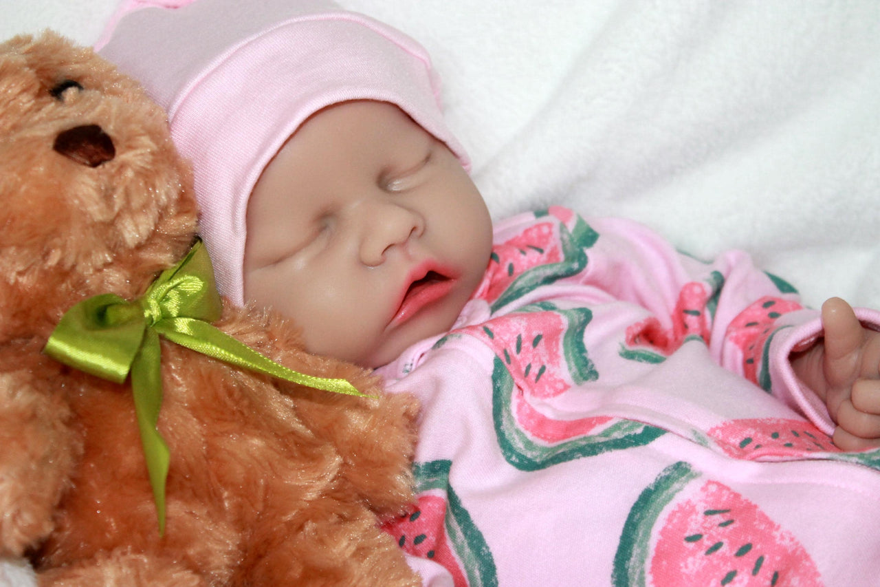 Infant doll lying on a blanket alongside a plush teddy bear.