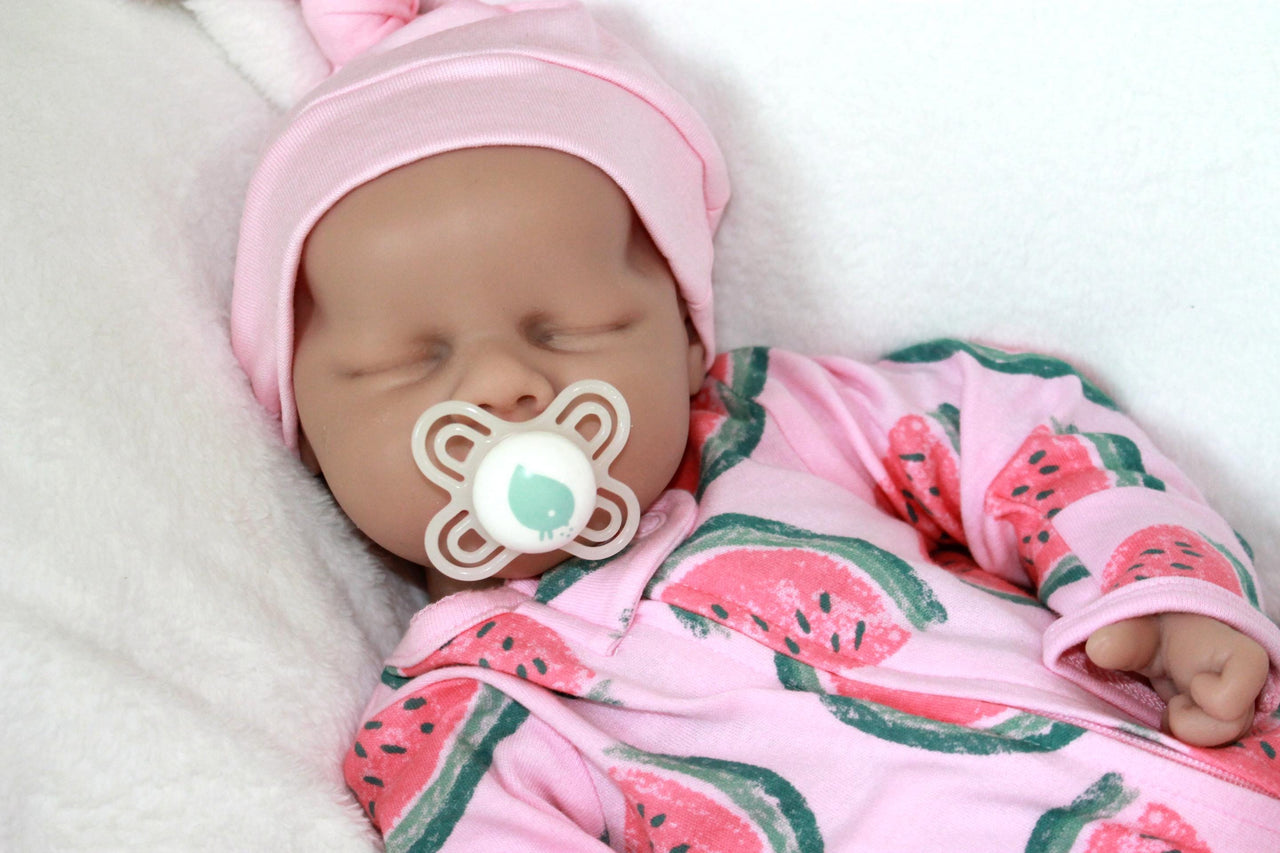 A baby doll holding a pacifier, dressed in a colorful outfit, with a gentle expression on its face.