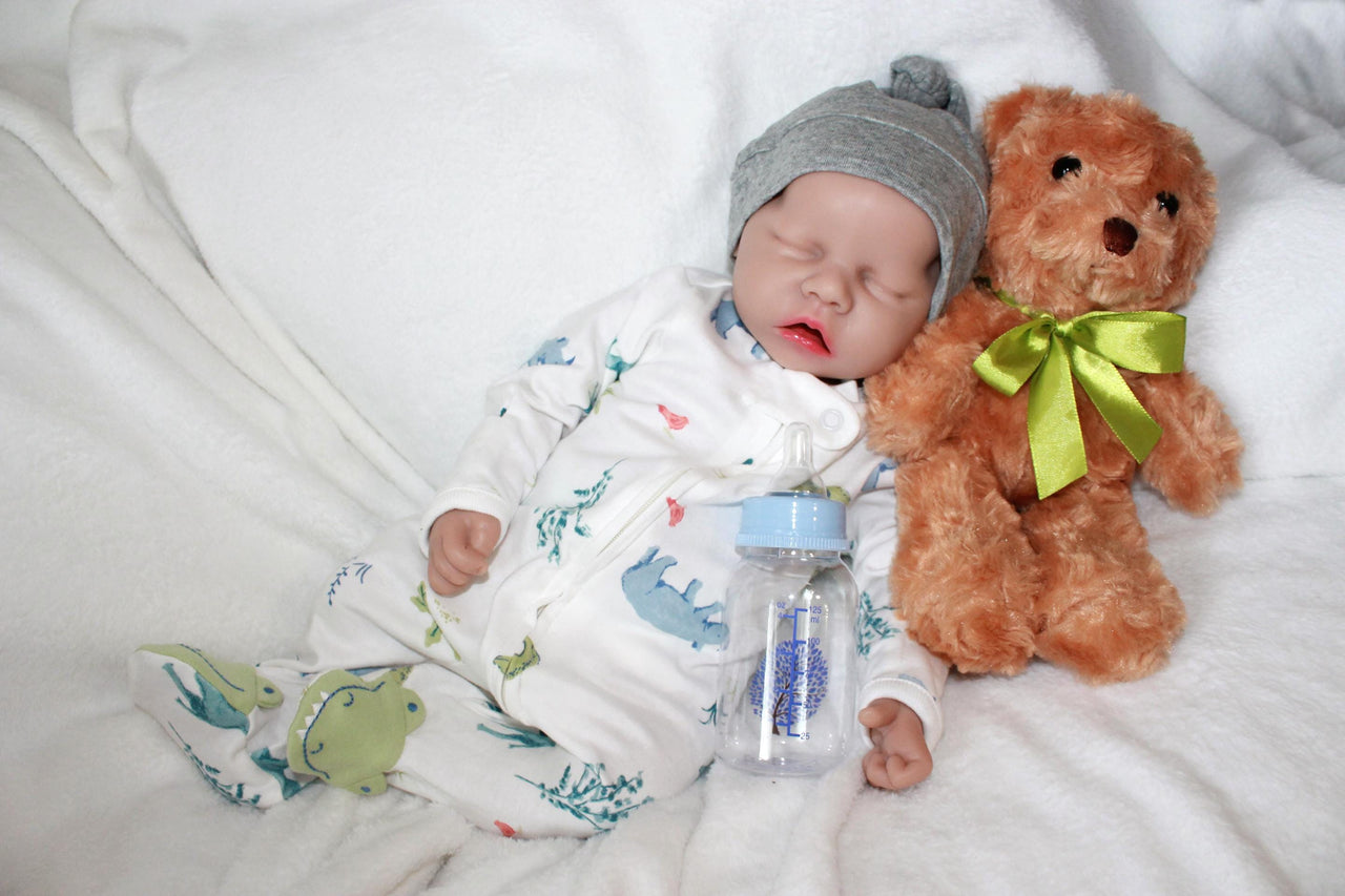 A baby doll positioned on a blanket, featuring a pacifier next to it.