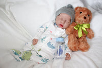 Thumbnail for A baby doll positioned on a blanket, featuring a pacifier next to it.