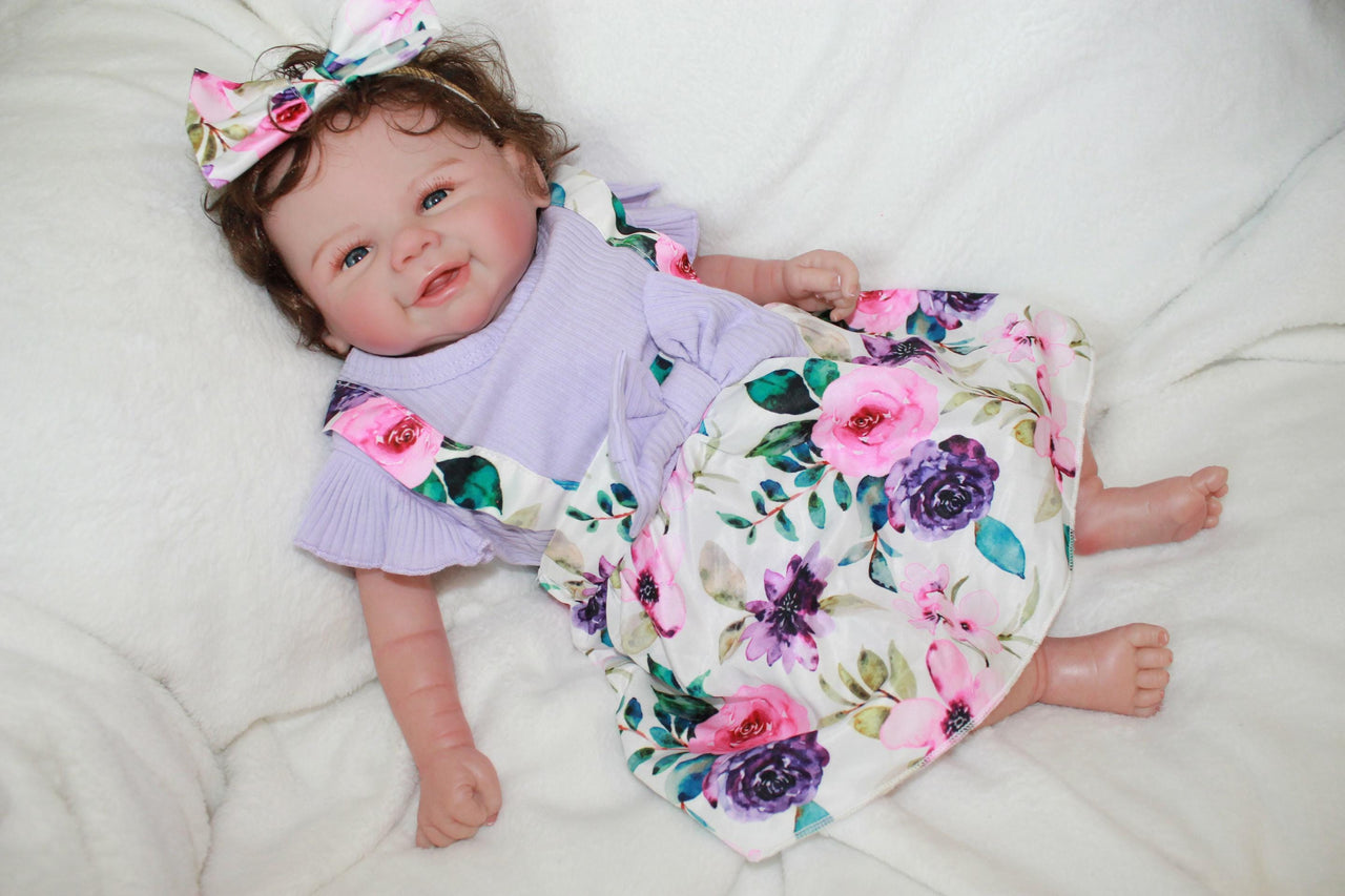 A baby doll dressed in a purple dress and adorned with a flower headband.