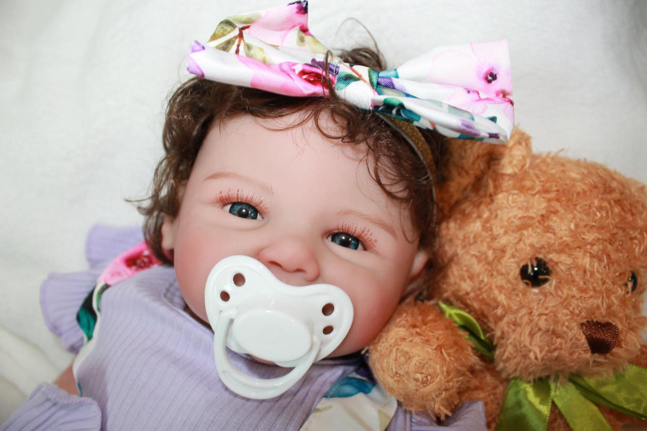 A baby doll dressed in a purple dress and adorned with a flower headband.