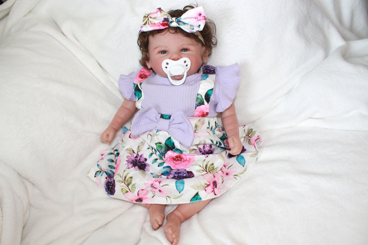 A baby doll wearing a purple dress and a decorative flower headband.