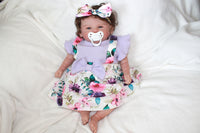 Thumbnail for A baby doll wearing a purple dress and a decorative flower headband.