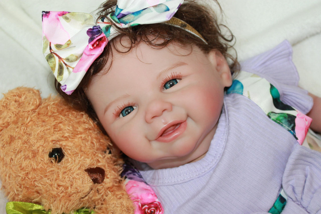 A baby doll wearing a purple dress and a decorative flower headband.