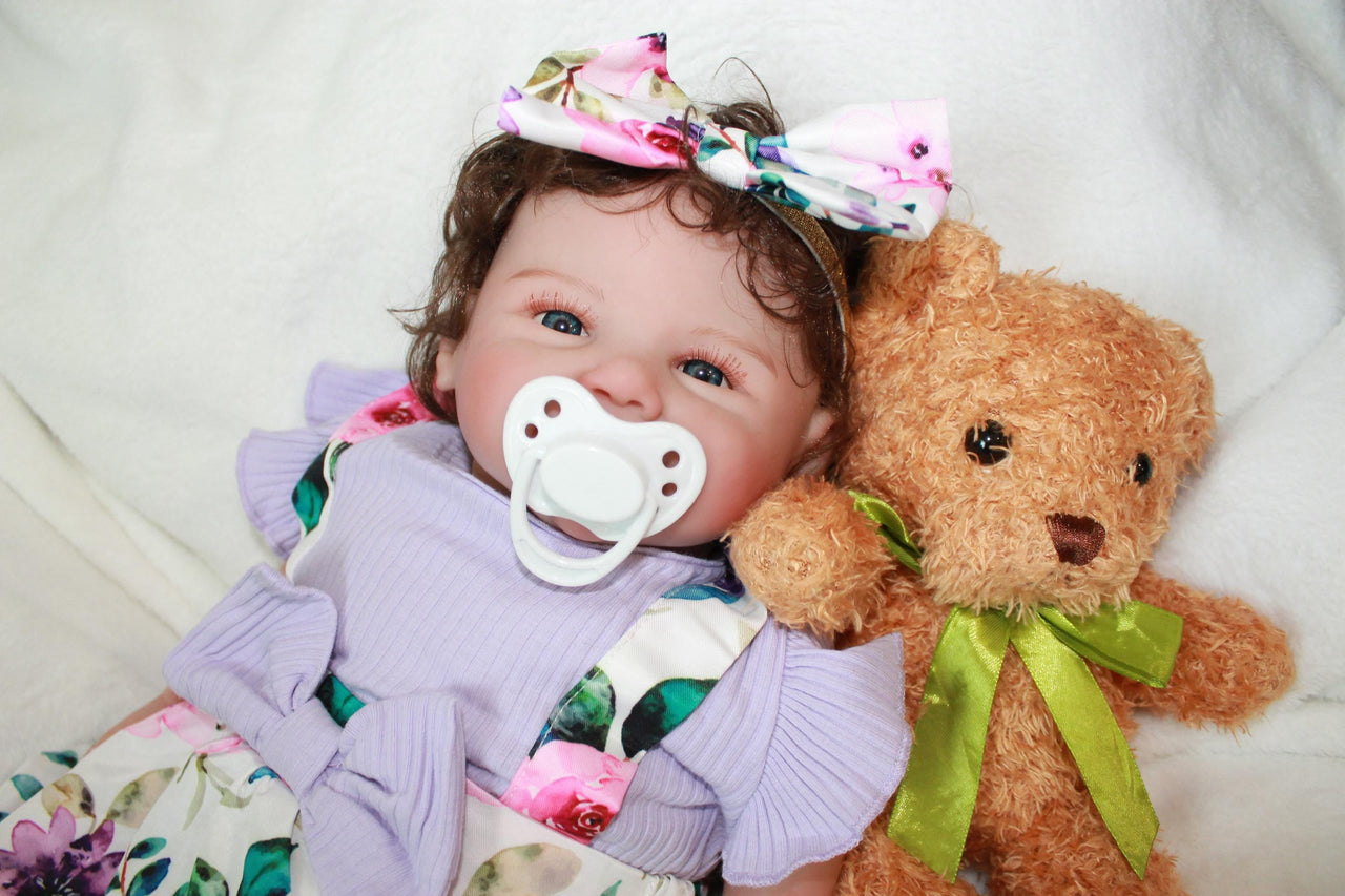 A baby doll wearing a purple dress and a decorative flower headband.