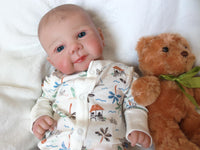 Thumbnail for A baby doll rests on a white blanket beside a soft teddy bear, creating a cozy and playful scene.