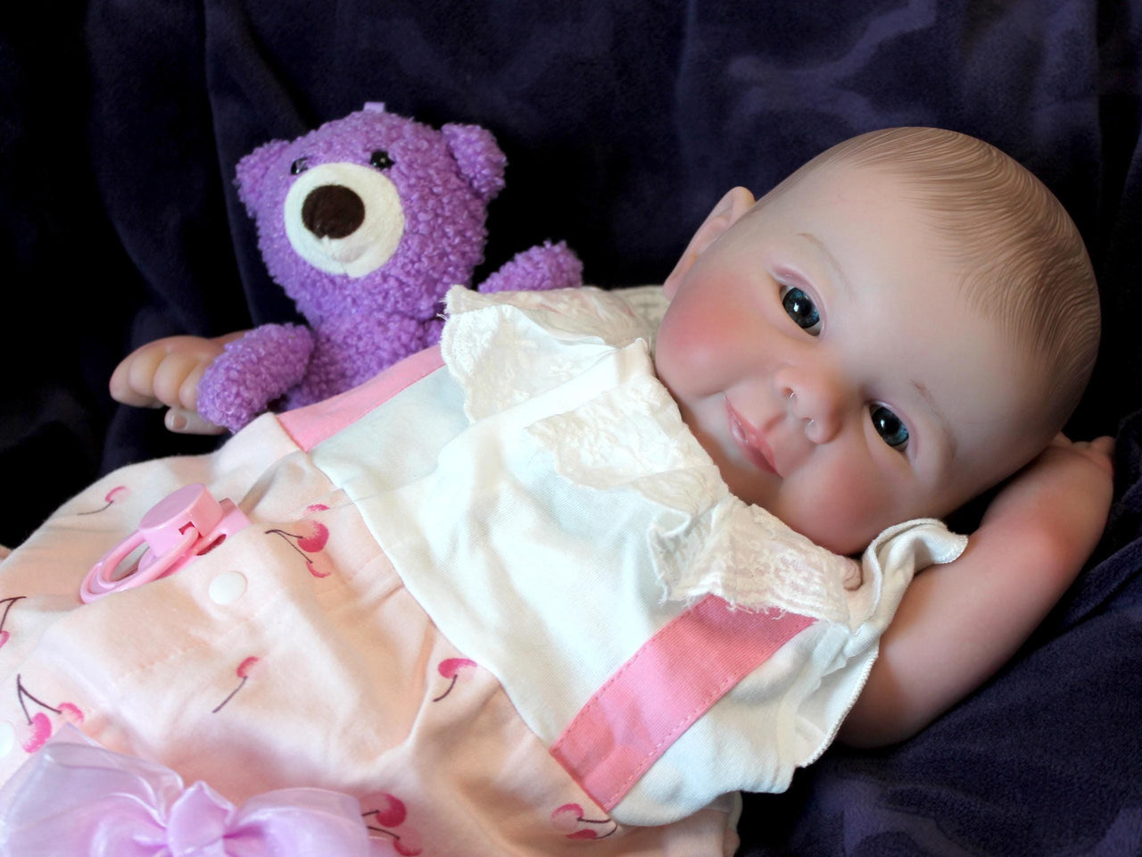 A baby doll resting on a purple sheet, showcasing its soft features and delicate clothing.