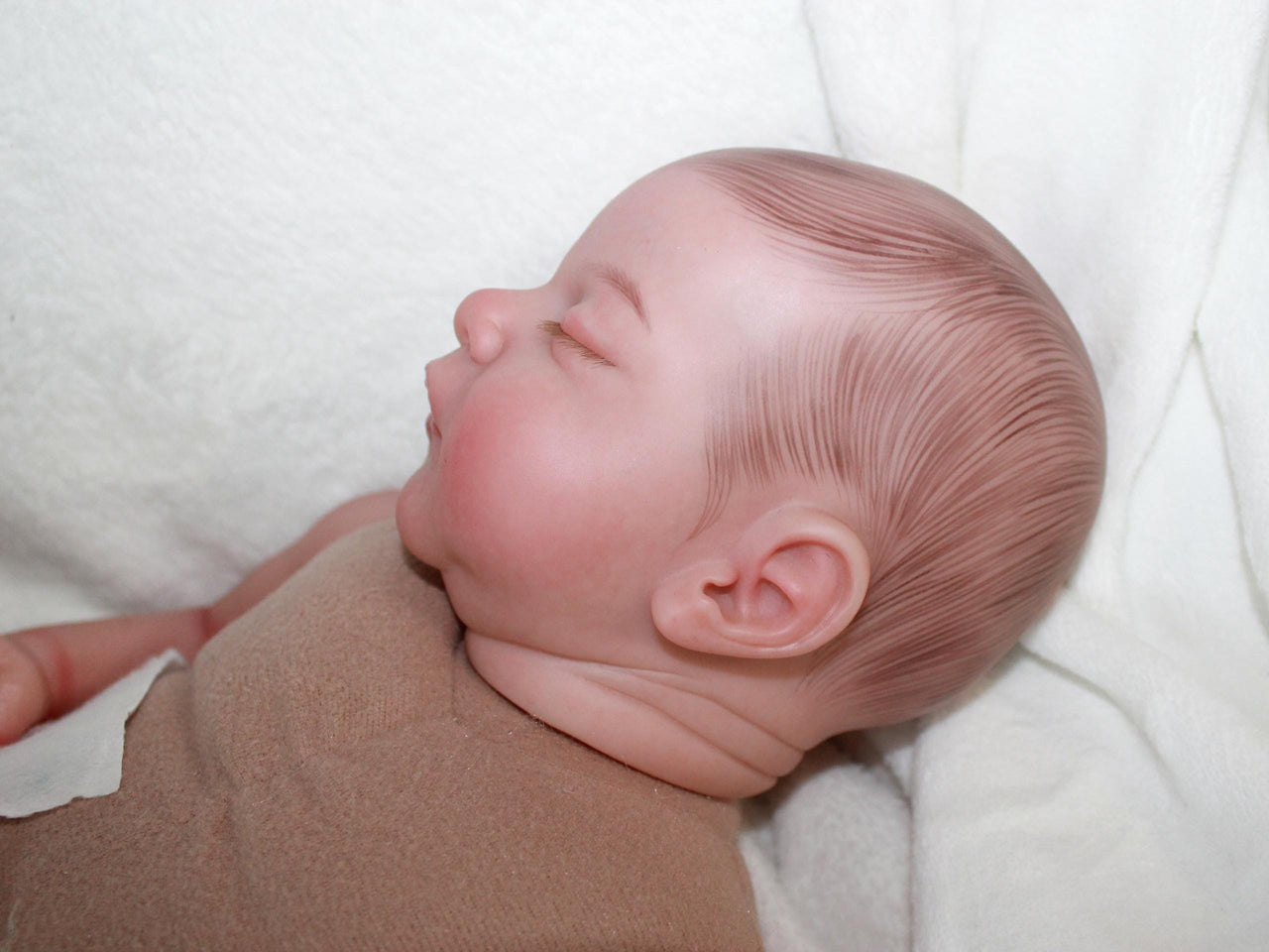 A sleeping baby doll rests on a fluffy white blanket, evoking a sense of calm and innocence.