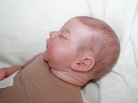Thumbnail for A sleeping baby doll rests on a fluffy white blanket, evoking a sense of calm and innocence.
