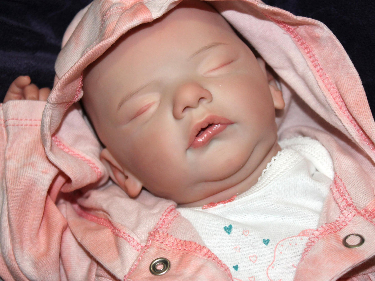 A baby doll lies asleep on a pristine white blanket, embodying tranquility and comfort.