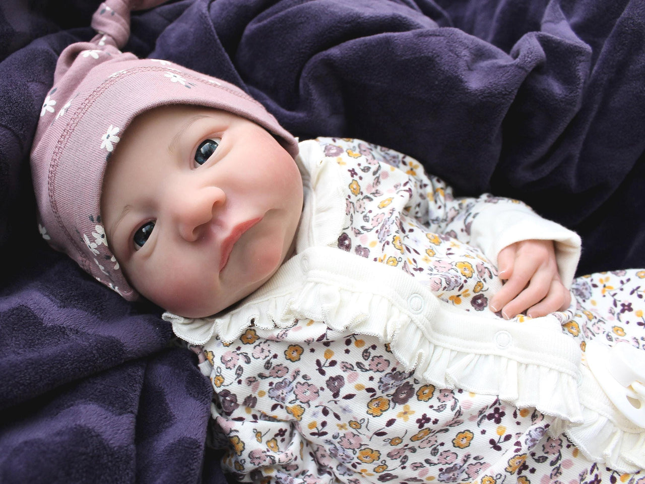 A baby dressed in floral rests on a cozy blanket, with a peaceful expression