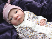 Thumbnail for A baby dressed in floral rests on a cozy blanket, with a peaceful expression