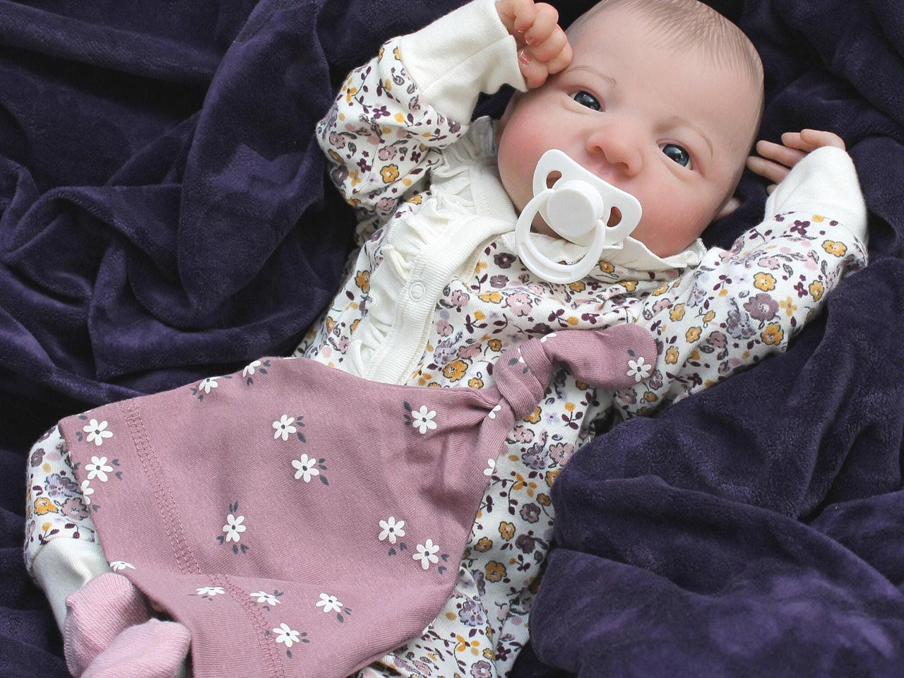 A baby dressed in floral rests on a cozy blanket, with a peaceful expression