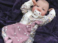 Thumbnail for A baby dressed in floral rests on a cozy blanket, with a peaceful expression
