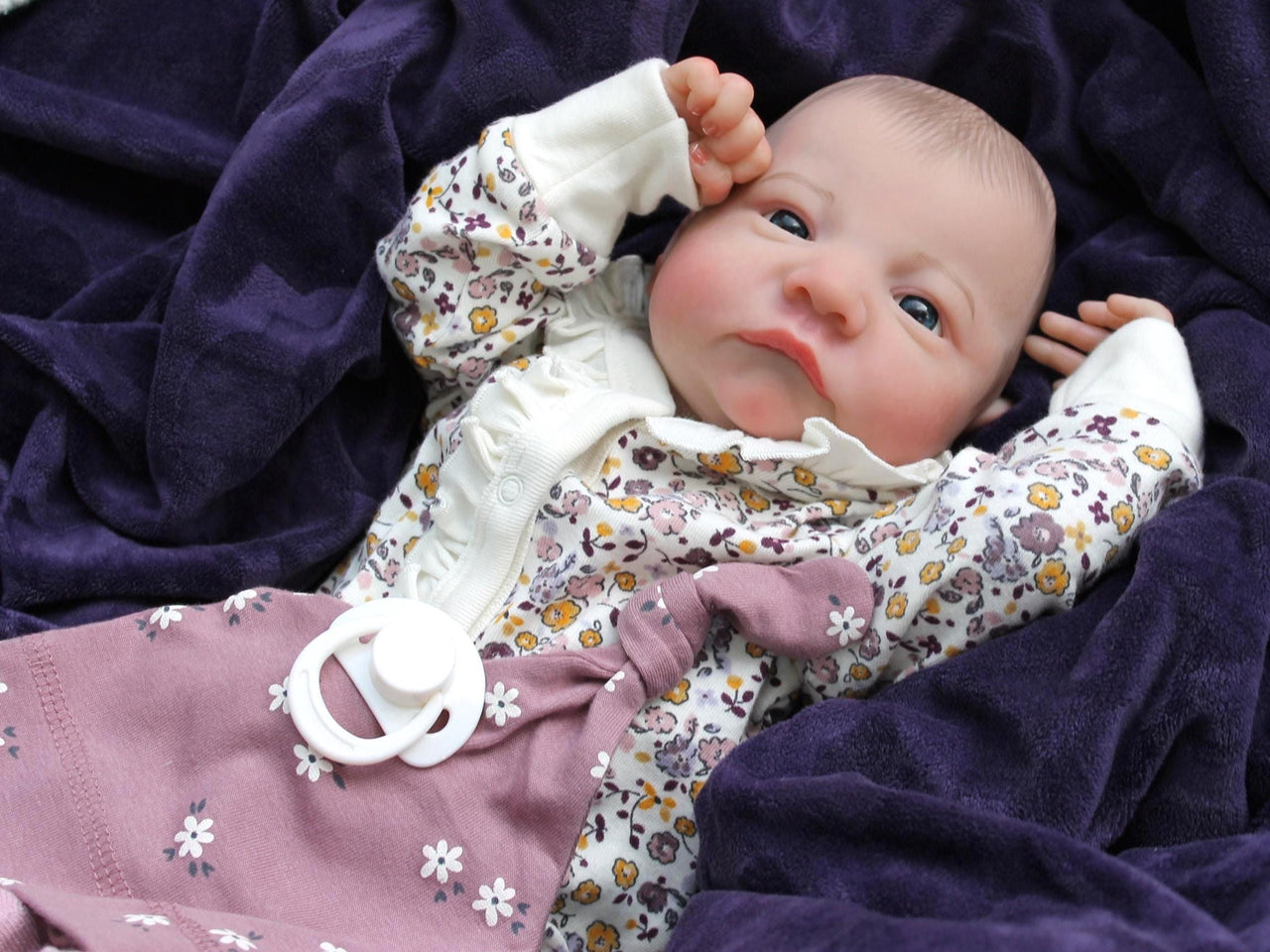 A baby wearing a floral outfit is comfortably lying on a blanket, surrounded by a serene atmosphere.
