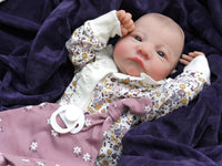 Thumbnail for A baby wearing a floral outfit is comfortably lying on a blanket, surrounded by a serene atmosphere.