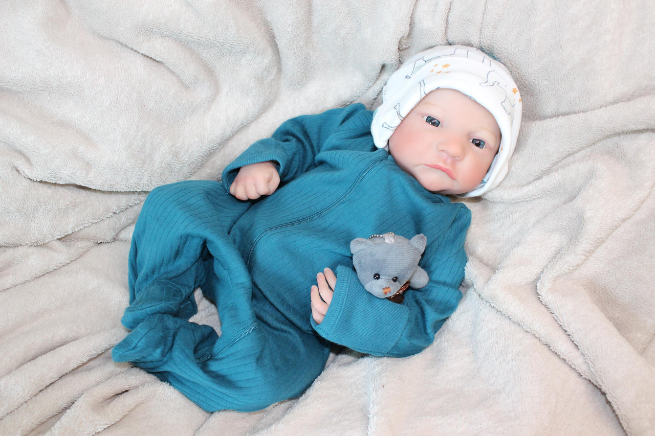 A baby wearing a blue outfit is comfortably lying on a blanket, surrounded by a serene atmosphere.