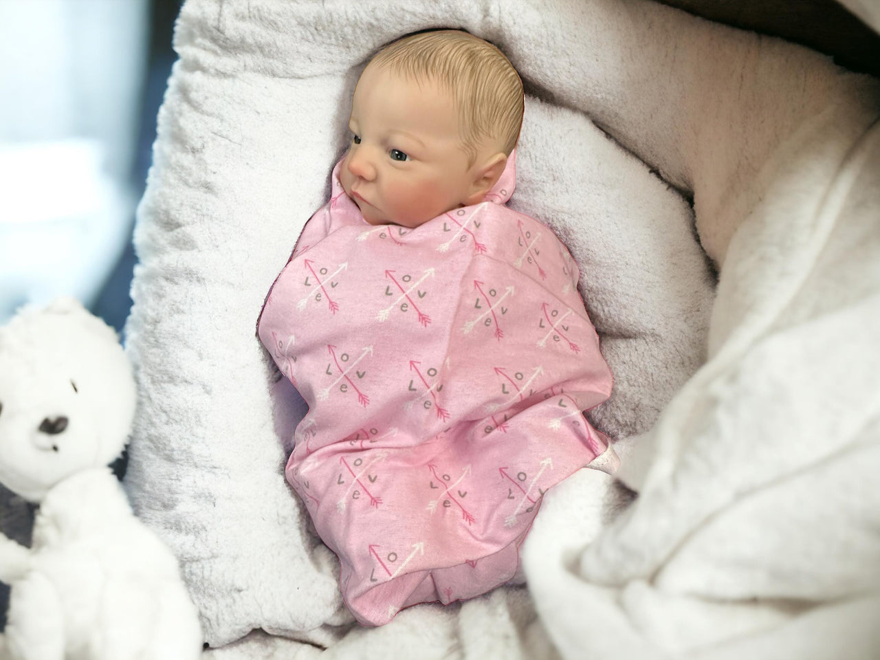 A baby wearing a pink blanket is comfortably lying on a blanket, surrounded by a serene atmosphere.