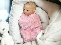 Thumbnail for A baby wearing a pink blanket is comfortably lying on a blanket, surrounded by a serene atmosphere.