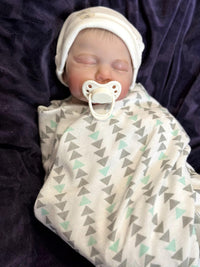 Thumbnail for A baby doll lying on a cozy blanket, with a pacifier placed nearby.