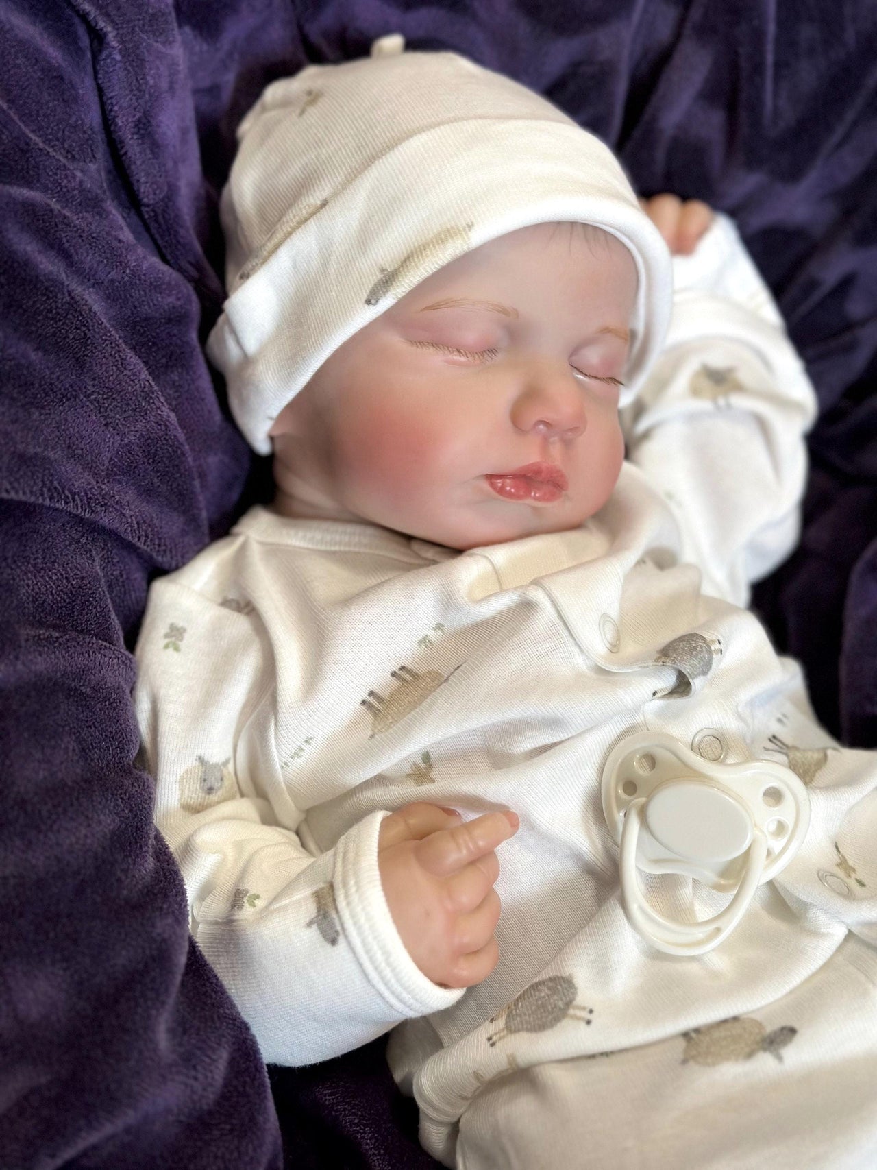 A baby doll rests on a soft blanket, showcasing its delicate features and clothing.