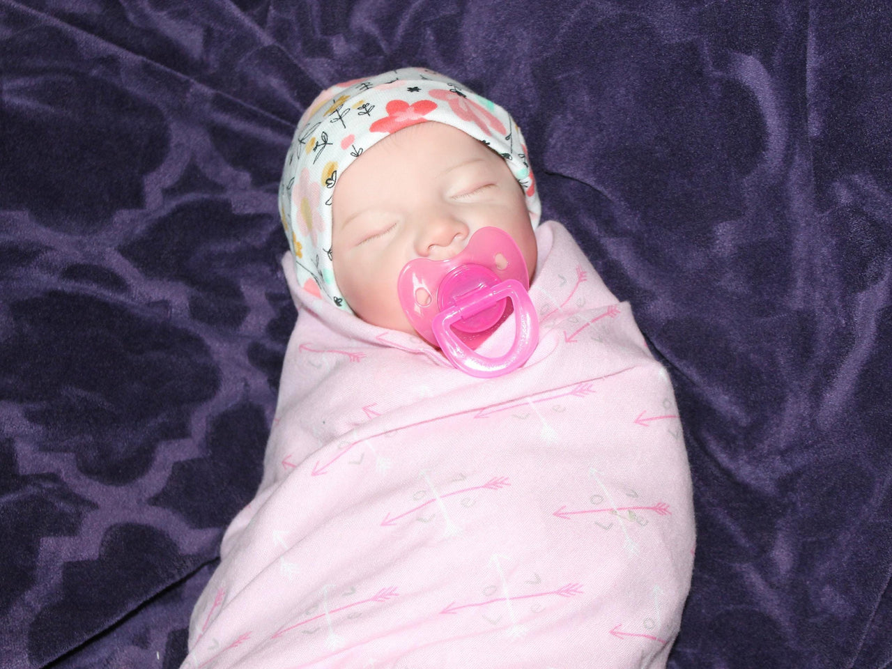 A baby in cozy pink blanket, resting on their back with a calm demeanor.