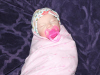 Thumbnail for A baby in cozy pink blanket, resting on their back with a calm demeanor.