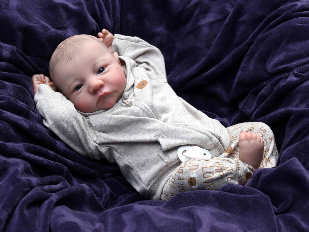 A baby doll resting on a soft blanket, showcasing its delicate features and clothing.