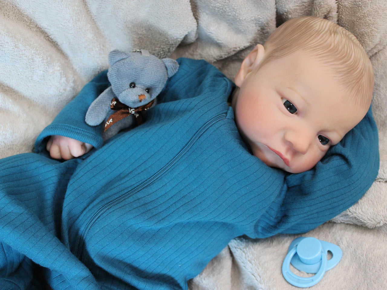 A baby doll rests on a soft blanket beside a cuddly teddy bear, creating a cozy and playful scene.