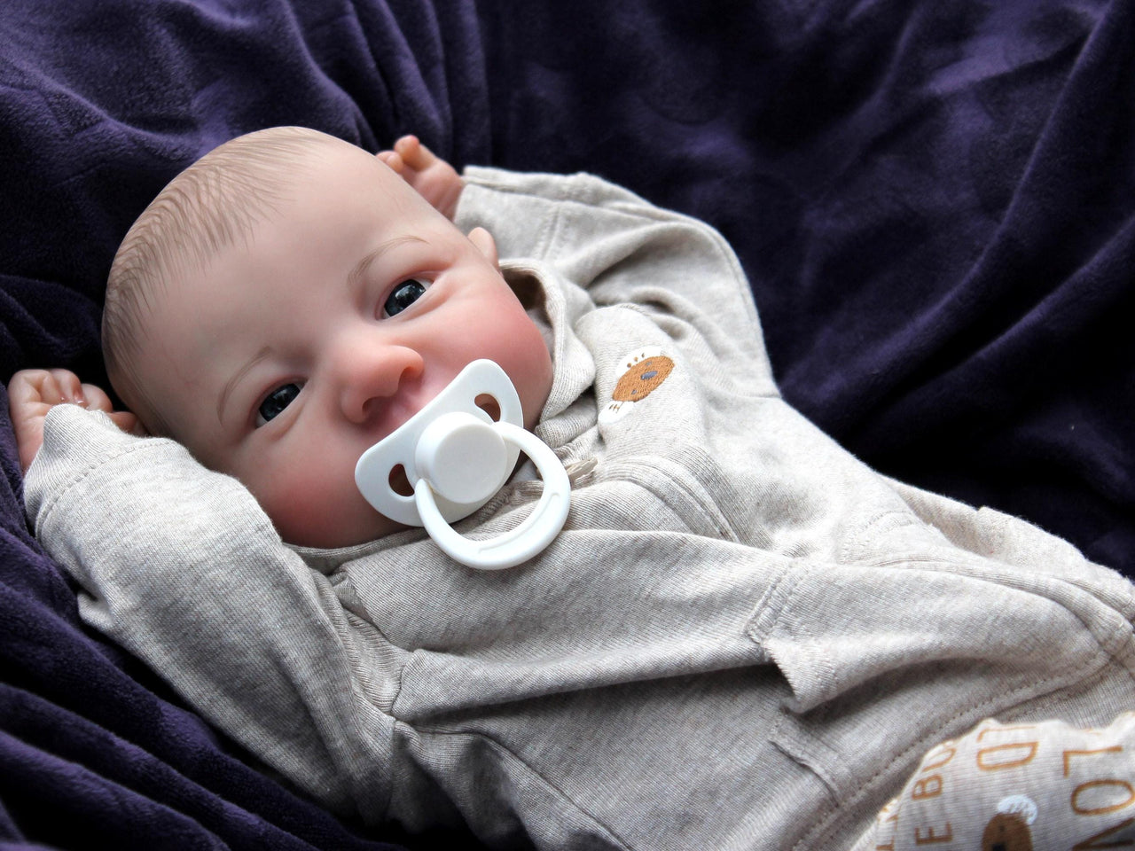 A baby doll resting on a soft blanket, showcasing its delicate features and clothing.