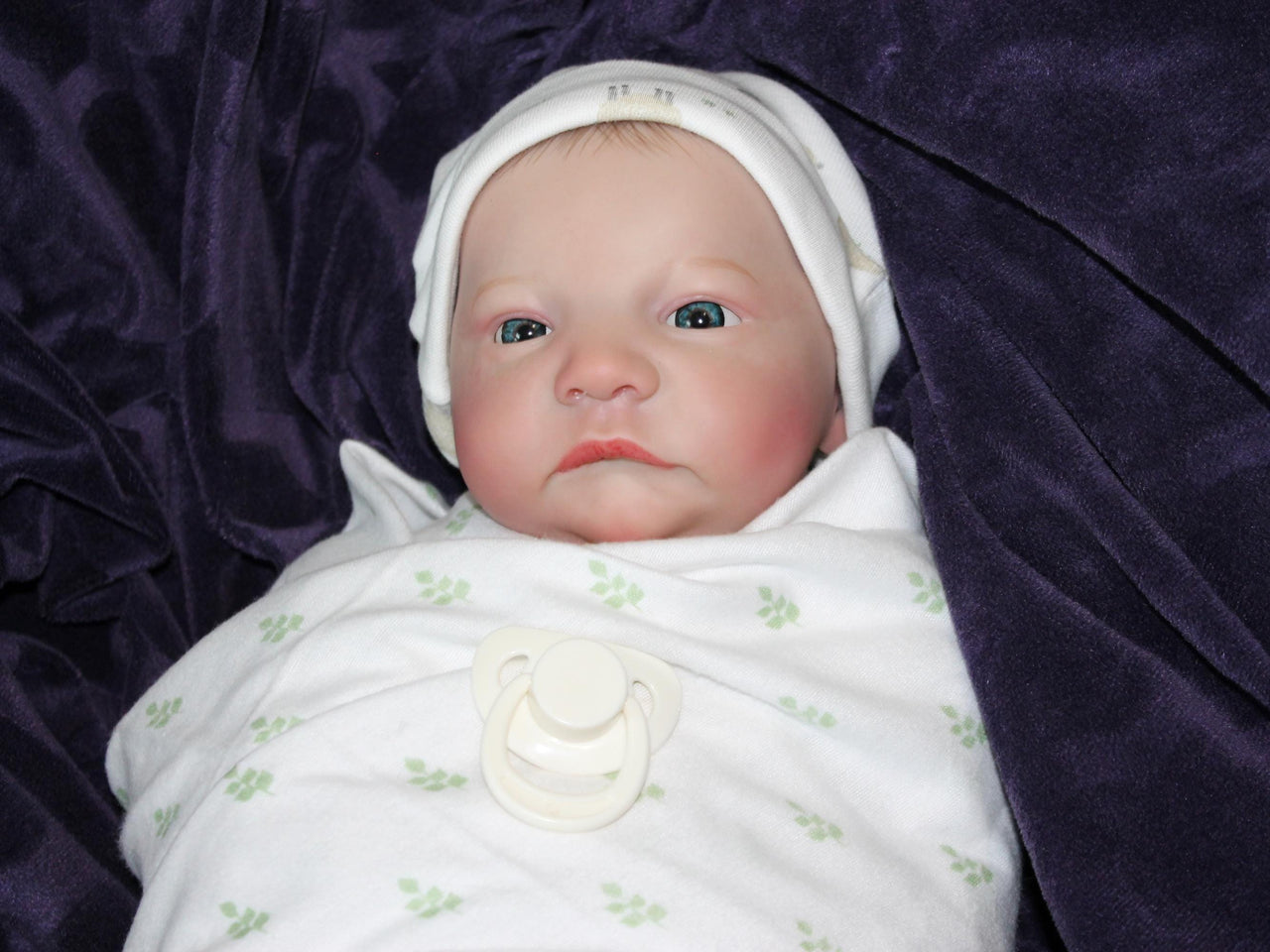 An infant wearing a hat, comfortably resting on a colorful blanket, exuding a sense of tranquilit