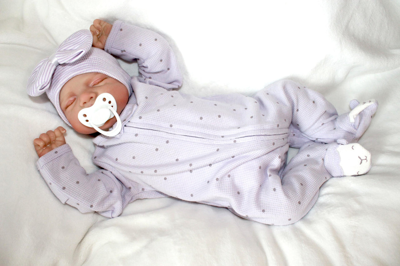 A baby doll with a pacifier lies on a bed, showcasing its soft features and gentle expression.