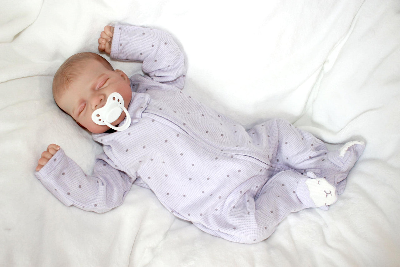 A baby doll with a pacifier lies on a bed, showcasing its soft features and gentle expression.