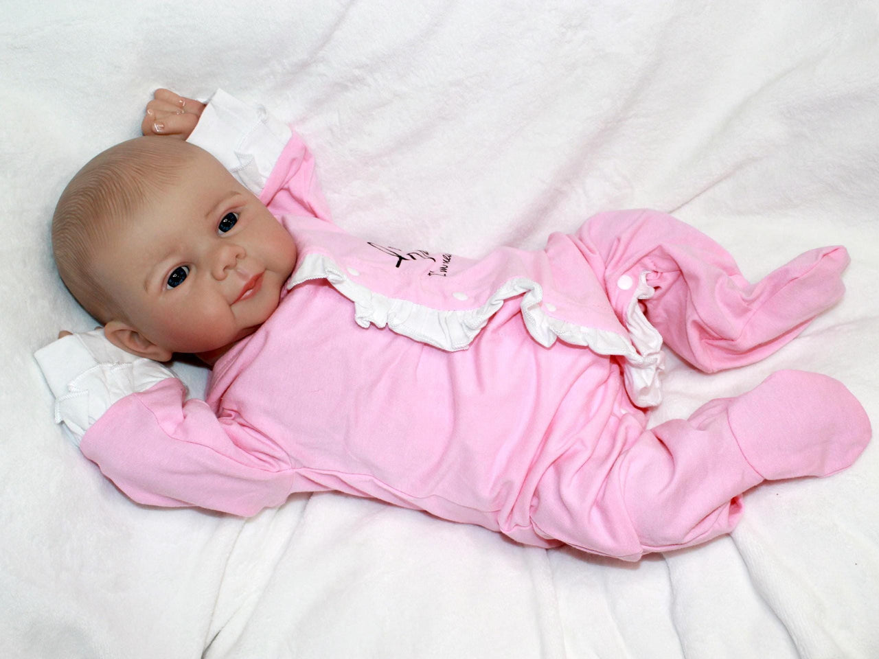 A baby doll lying on a pristine white sheet, emphasizing its adorable appearance and gentle colors.