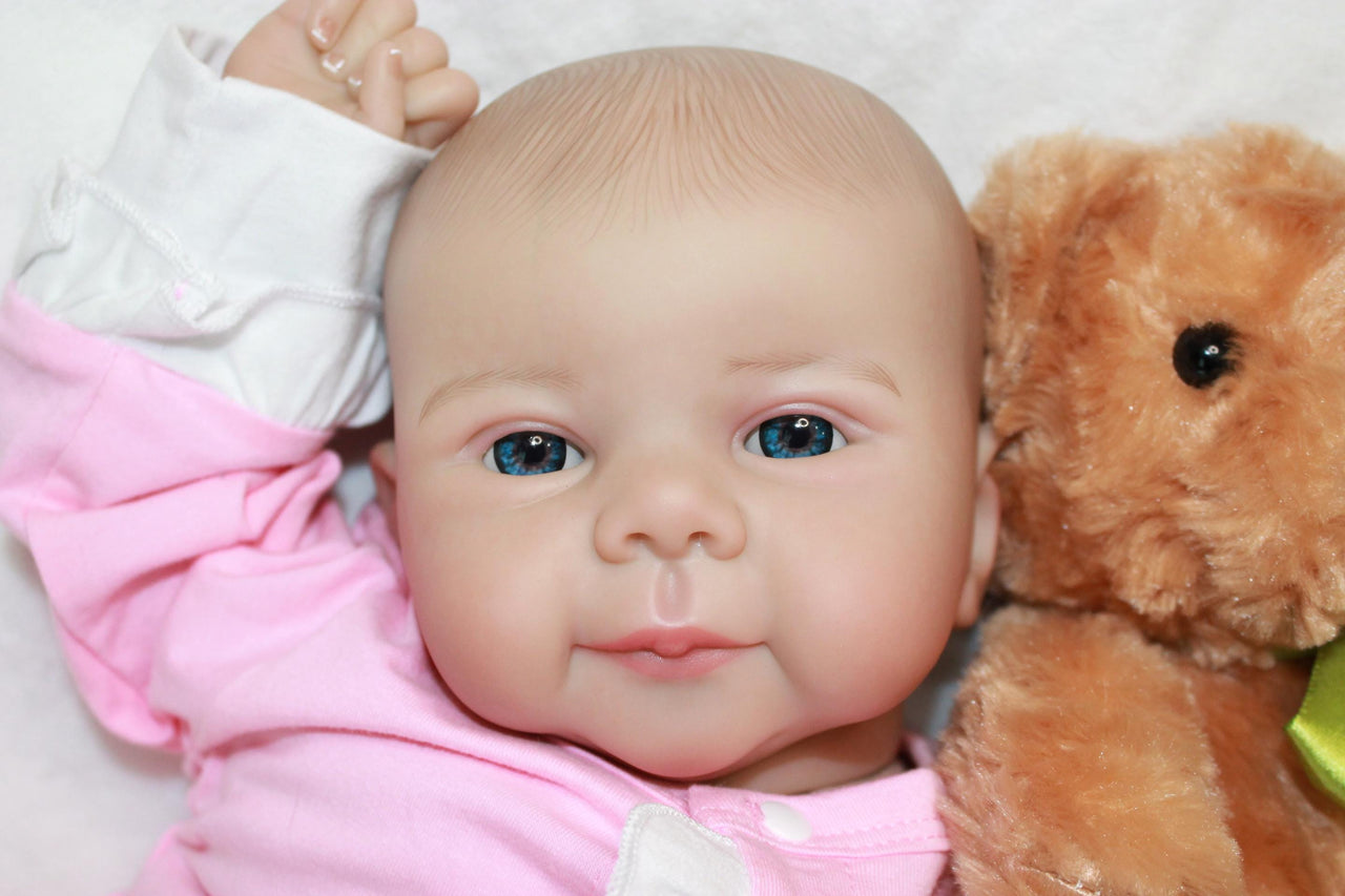 A baby doll positioned on a clean white sheet, highlighting its charming design and soft textures.