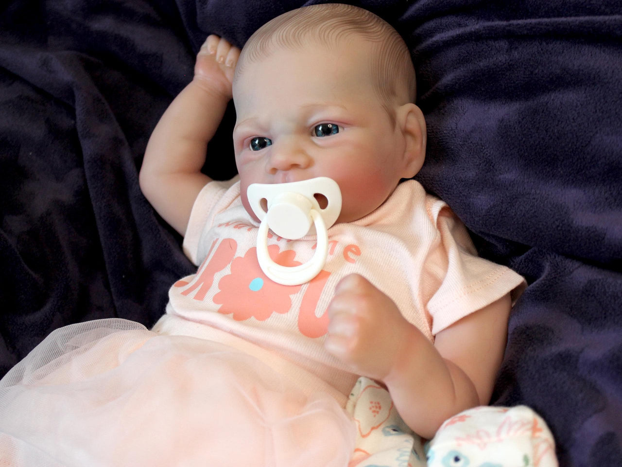 A baby doll with a pacifier rests on a soft blanket, showcasing its delicate features and gentle expression.