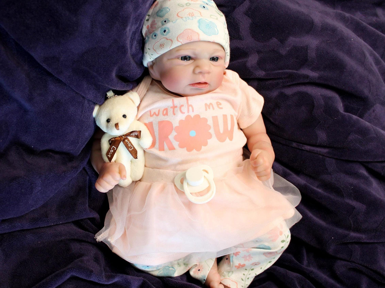 A baby doll dressed in a pink shirt and wearing a hat, sitting against a soft background.