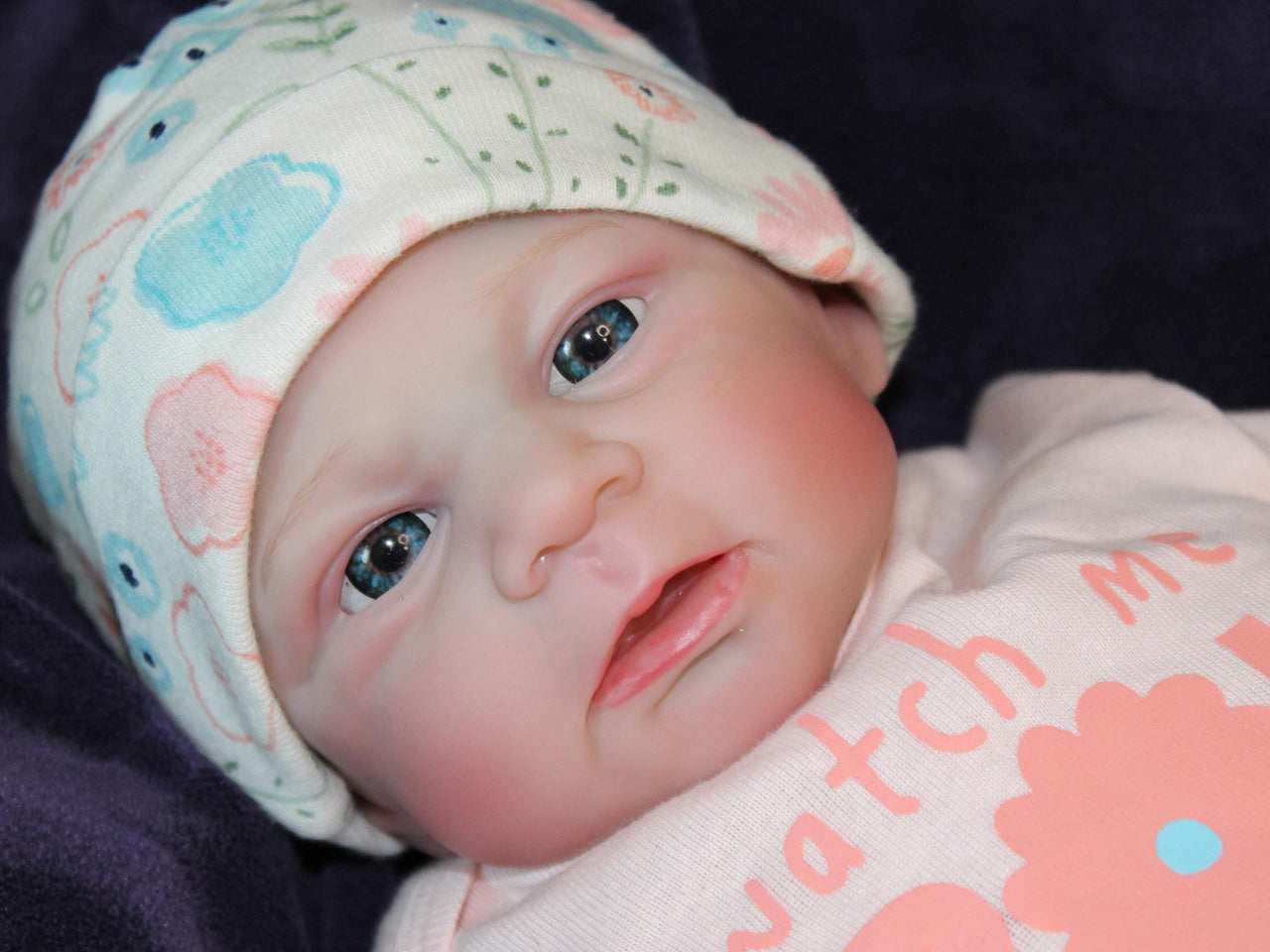 A baby doll with a hat and a pink shirt, posed cutely on a light-colored surface.
