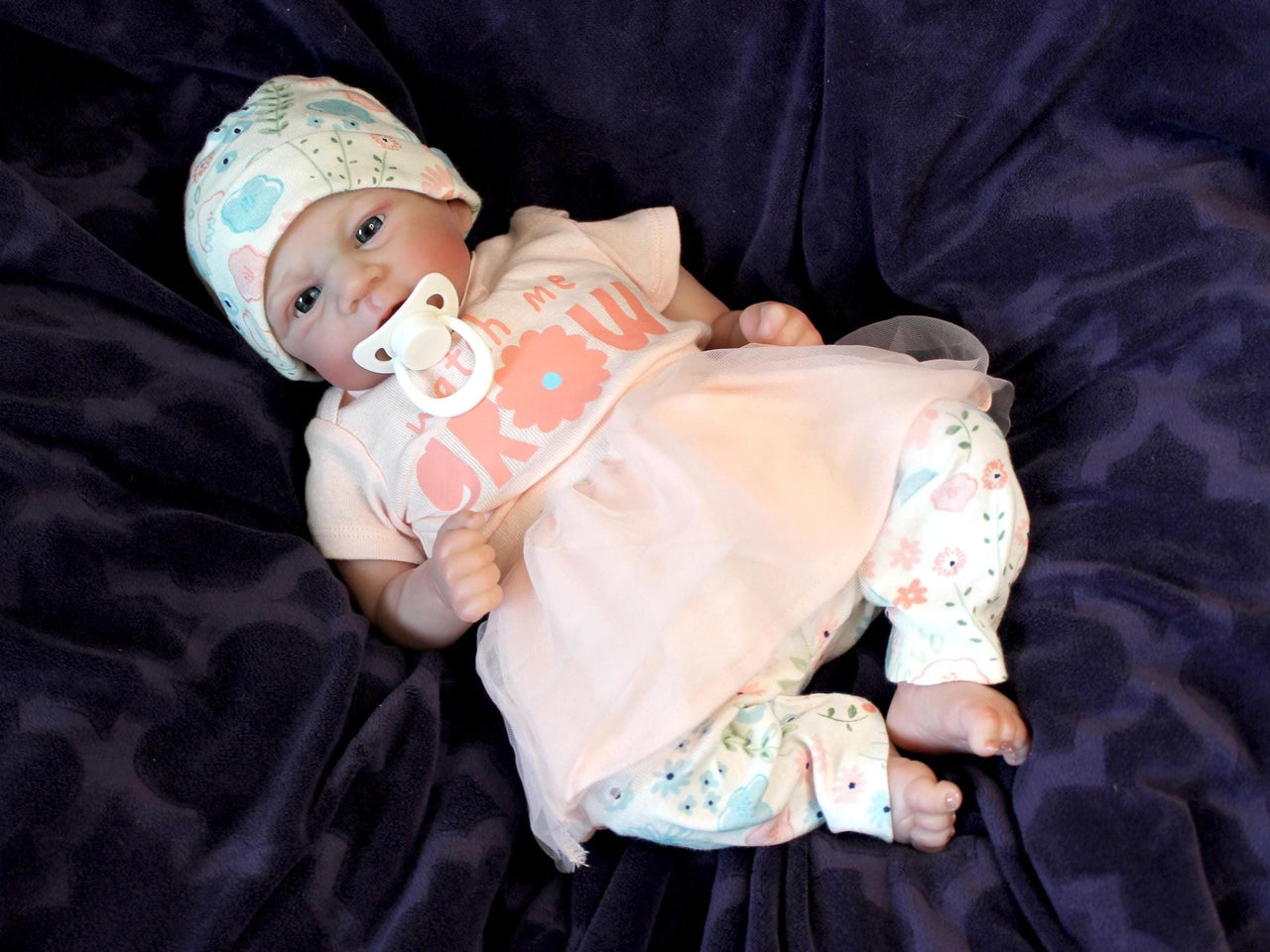 A baby doll with a pacifier rests on a soft blanket, showcasing its delicate features and gentle expression.