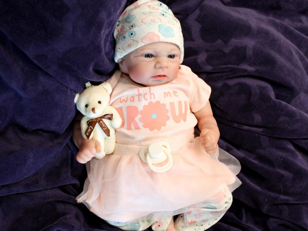 A baby doll in a pink dress and hat, posed cutely with a gentle smile, highlighting its charming design.