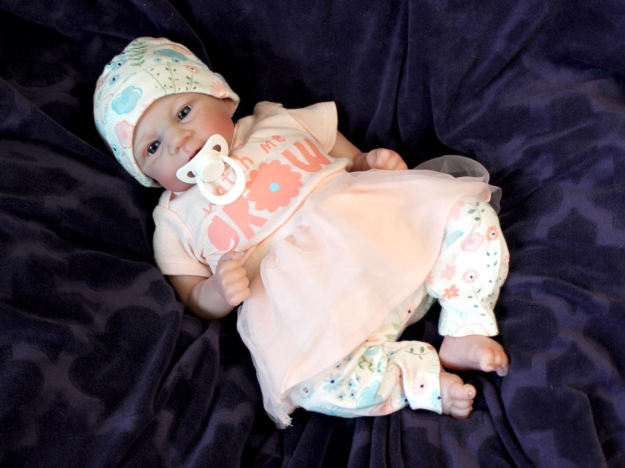 A baby doll with a pacifier lies on a cozy blanket, highlighting its charming design and soothing presence.
