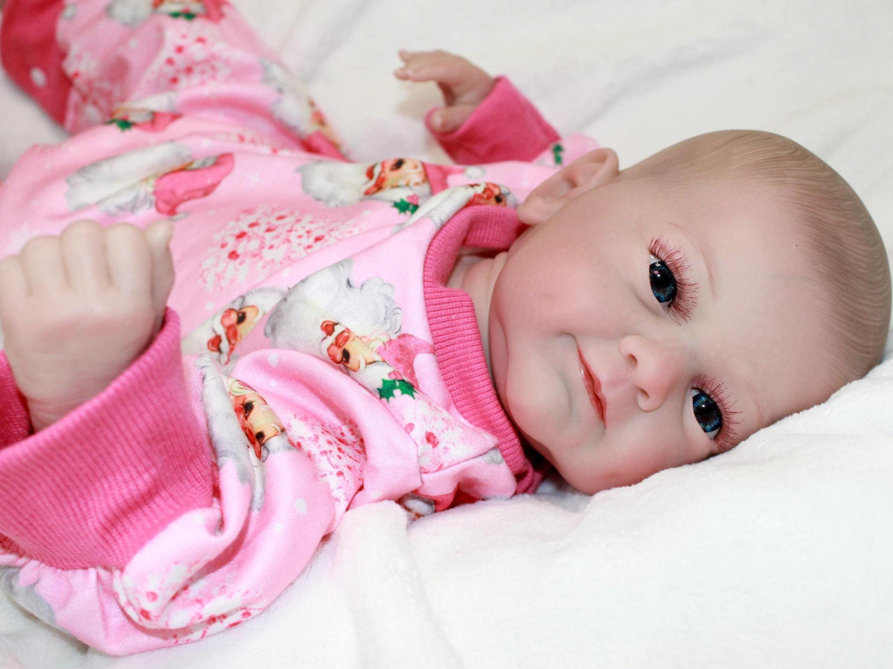 A baby doll wearing pink pajamas is positioned on a bed, highlighting a serene and nurturing environment.
