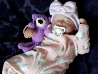 Thumbnail for A baby doll positioned on a plush purple couch, highlighting its charming design and vibrant outfit.
