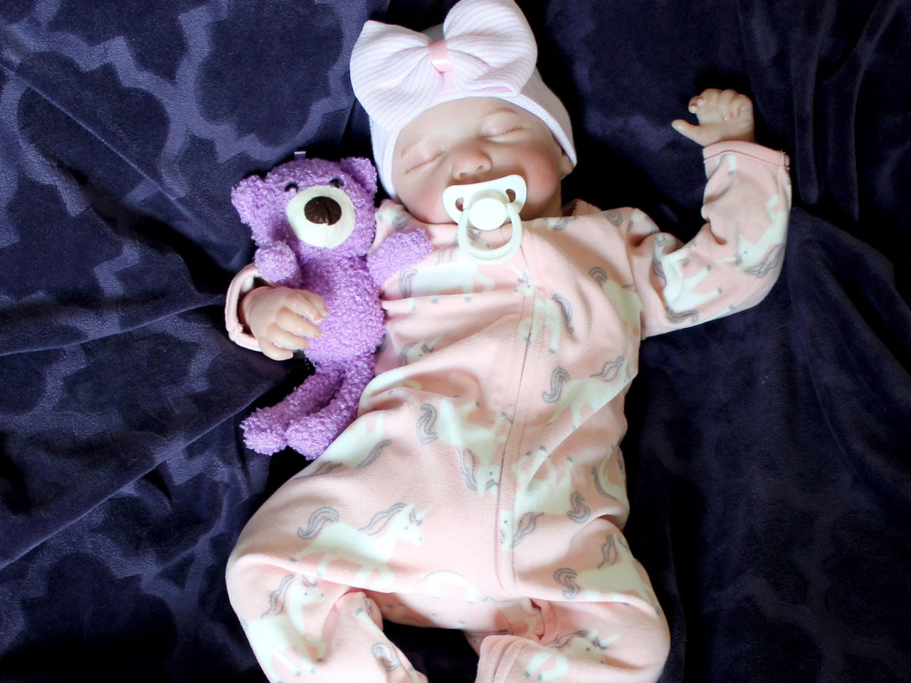 A baby doll positioned on a plush purple couch, highlighting its charming design and vibrant outfit.