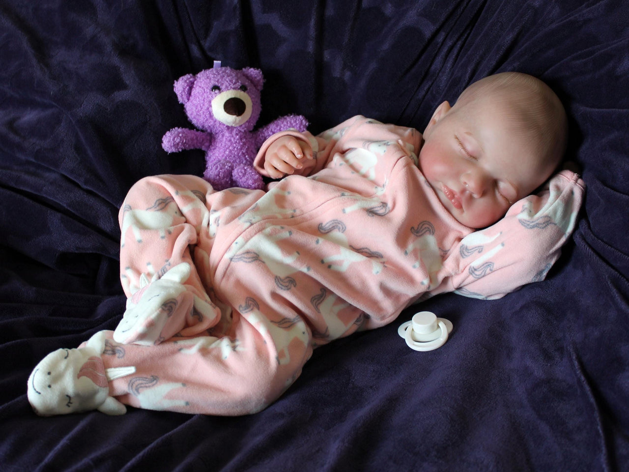 A baby doll lying on a cozy purple couch, emphasizing its cute appearance and colorful attire.