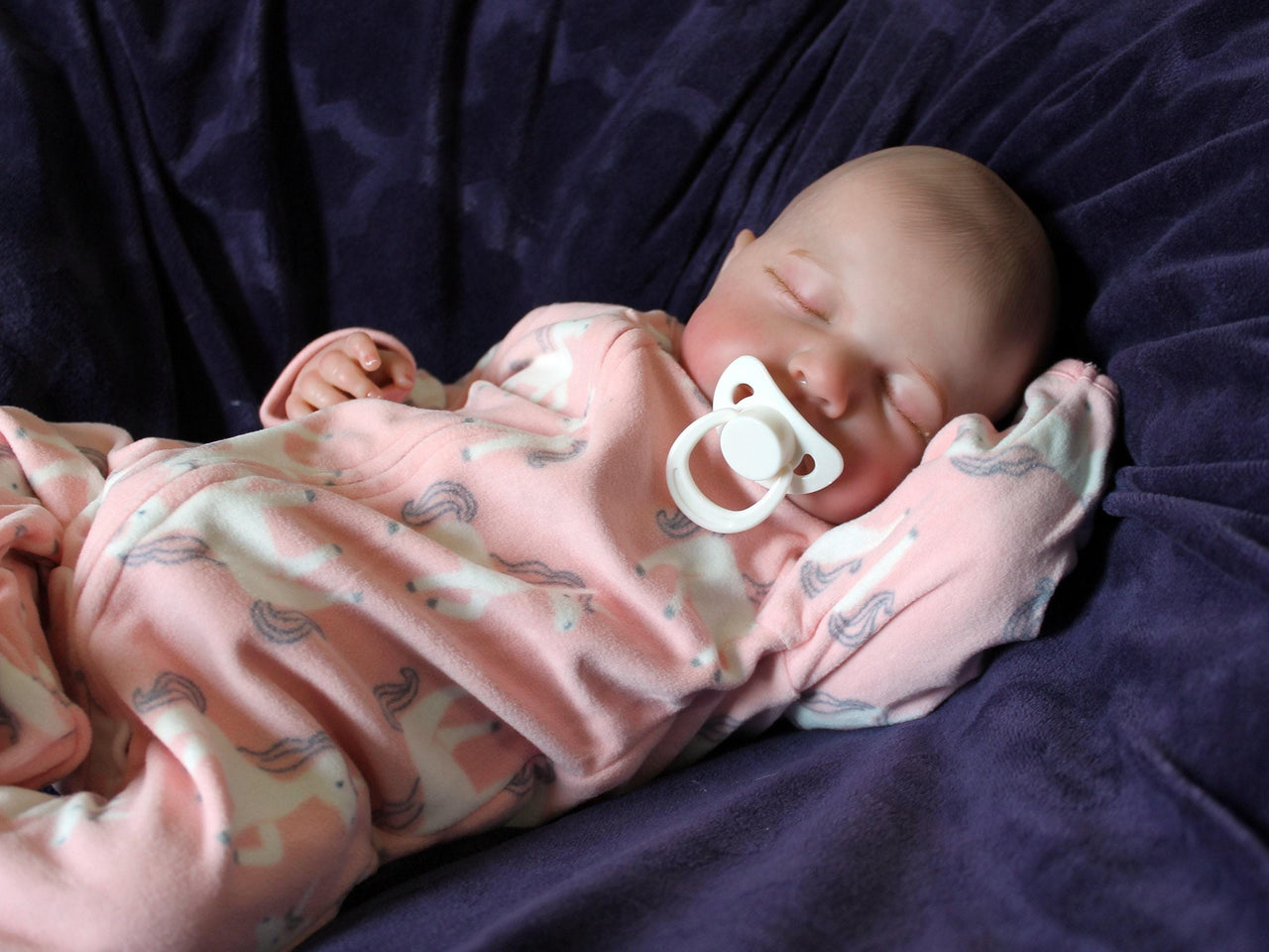 A baby doll lying on a cozy purple couch, emphasizing its cute appearance and colorful attire.